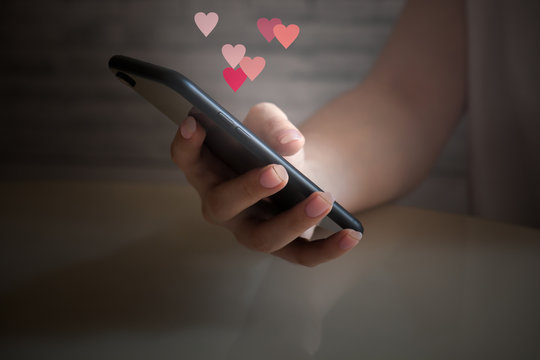 Woman hand holding mobile phone with glowing screen with different virtual hearts, love symbol , valentine day concept, virtual life and emotions, real life concept