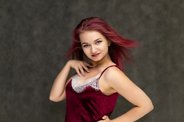 Obraz premium Concept portrait of a pretty sexy girl with purple hair in beautiful red lingerie on a gray background. She smiles, happy with life, happy. Hair flying, front view. Made in a studio.