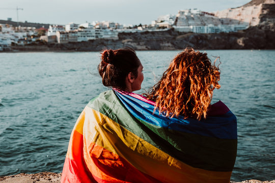 .Young and beautiful lesbian couple proudly celebrating their sexuality at sunset. They hold the rainbow flag of the lgtbi collective, happy and carefree. Love is love.