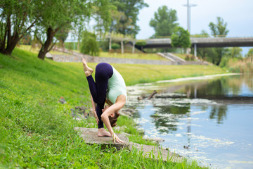 Slim young brunette yogi performs no complicated yoga exercises on the green grass in summer...