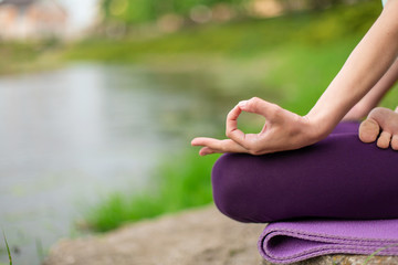 Yoga woman practicing yoga lesson, breathing, meditation, doing exercise Ardha Padmasana, half lotus pose with mudra gesture, closeup in summer on nature against the background of water