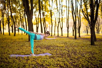 Thin brunette girl plays sports and performs yoga poses in autumn park on a sunset background....