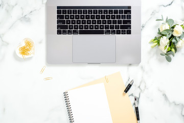 Flat lay home office desk. Women workspace with laptop computer, white flowers bouquet, golden accessories, diary on marble surface. Top view feminine background.