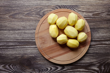 Peeled potatoes on wooden cutting board on brown table. Cooking food from natural products. Root vegetable. Raw ingredient: uncooked whole potatoes