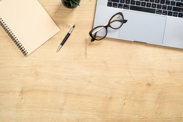 Wood office desk table with blank notebook, laptop computer, pen, glasses, succulent plant. Minimal flat lay style composition, top view, overhead. Business woman workspace concept.