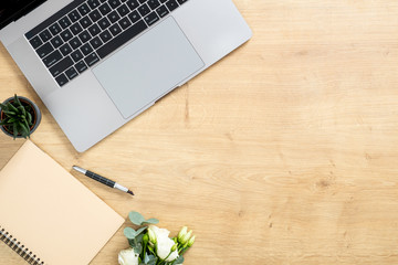 Modern wooden office desk table with laptop computer, paper notepad, pen, succulent plant, bouquet of roses flowers. Minimal flat lay style composition with copy space, top view. Business concept.