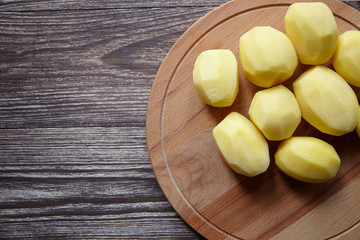 Peeled potatoes on wooden cutting board on brown table. Cooking food from natural products. Root vegetable. Raw ingredient: uncooked whole potatoes