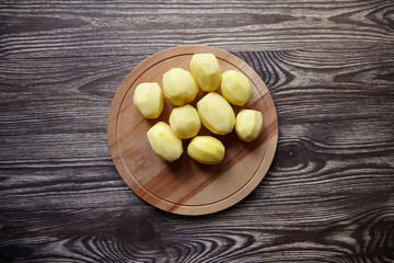 Peeled potatoes on wooden cutting board on brown table. Cooking food from natural products. Root vegetable. Raw ingredient: uncooked whole potatoes