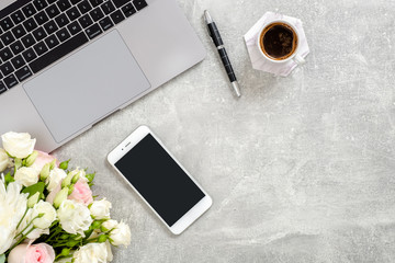 Minimalist home office desk with blank copy space mockup screen smartphone, laptop computer, coffee cup, flowers on concrete stone background. Flat lay, top view with copy space. Lifestyle blog banner
