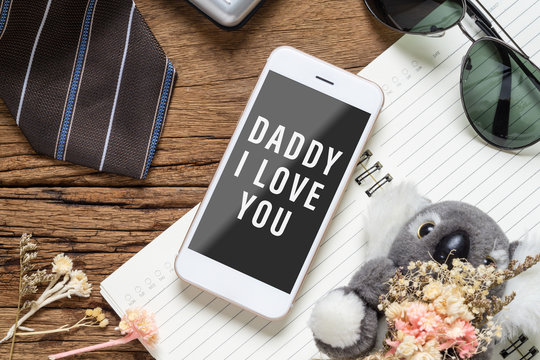 Father's day background concept. Mock up mobile phone for your artwork with Father's accessories items and daughter's toy on wood with Dady I love you messages on smartphone.