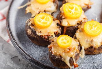 stuffed fried champignons with cheese, kumquats and green peas on a gray concrete background. side view, close up, macro.