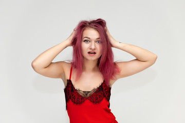 Fototapeta premium Concept portrait of a pretty sexy girl with purple hair in beautiful red lingerie on a white background. She smiles, happy with life, happy. Hair flying, front view. Made in a studio.