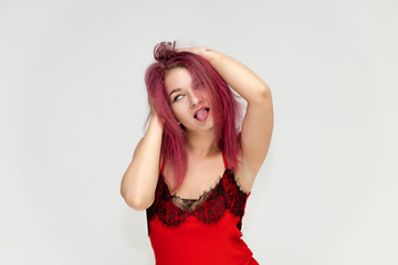 Fototapeta premium Concept portrait of a pretty sexy girl with purple hair in beautiful red lingerie on a white background. She smiles, happy with life, happy. Hair flying, front view. Made in a studio.