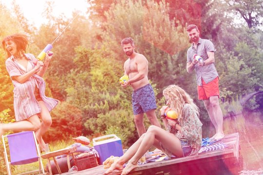 Tilt shot of cheerful couples enjoying with squirt guns on pier during summer