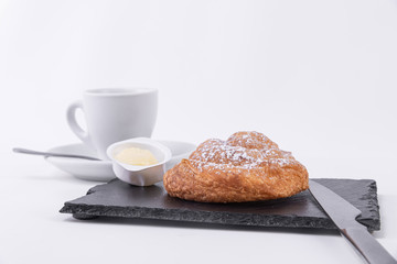 Tasty puff pastry roll with powdered sugar on top, butter spread and hot coffee