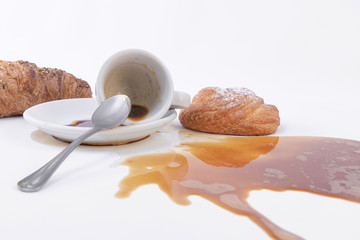 Spilled coffee and a roll of golden puff pastry with powdered sugar on top