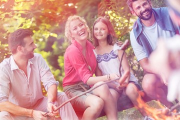 Fototapeta premium Tilt shot of happy family with male friend roasting sausages over campfire at park