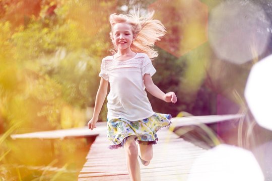 Smiling blond girl running on pier at lakeshore
