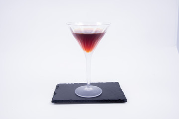 A red cocktail served in a glass cup on a black stone table insulated on a white background