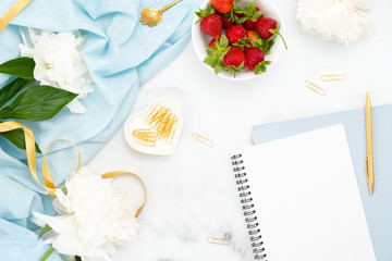 Flat lay feminine home office workspace with peony flowers, paper notepad and golden decorations on marble background. Top view women desk, summer fashion or beauty blog banner template.