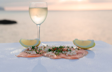 Luxurious dish - Smoked salmon with fresh lemon spread over a white dish accompanied by a glass of wine - Fresh salmon - Cut green celery - Cut white onion