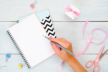 Female home office desk. Girl's hand writing a text message in blank diary. Beauty blogger...