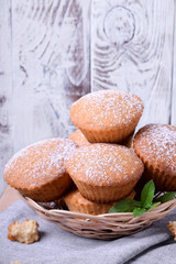 Fresh muffins topped with sugar powder in a wicker basket against the white wooden wall