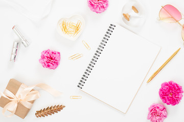 Flat lay home office desk. Top view blank paper notepad, pink rose flower buds, petals, female accessories, gift box on white background. Women desk, fashion blogger, beauty concept.