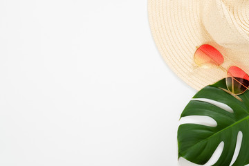 Minimal composition with beach straw hat, sunglasses and tropical Monstera palm leaf on white background. Flat lay, top view still life concept.