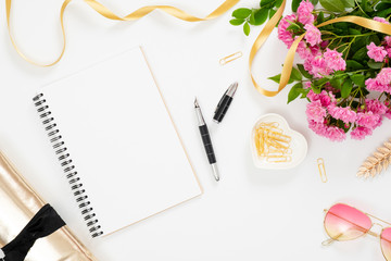 Modern home office desk workspace with blank paper notepad, feminine accessories, glasses, bouquet of pink rose flowers on white background. Flat lay female table, top view.