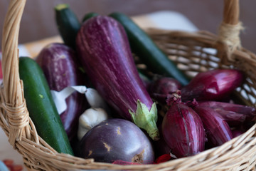 Wicker basket full of vegetables: aubergines, zucchini, onions and garlic