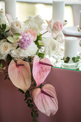 The wedding table setting for the newlyweds is decorated with fresh flowers of carnation, rose, anthurium and eucalyptus leaves. Silver candlesticks, white candles. Wedding floristry. Close-up details