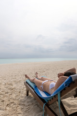 A young girl in a white bathing suit is lying on a lounger and sunbathing.