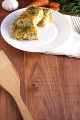 Delicious homemade casserole of zucchini, rice and cheese on a white plate on a wooden background.