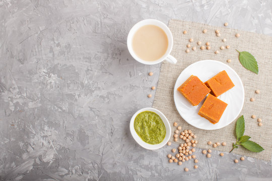 traditional indian candy burfi in white plate with mint chutney on a gray concrete background. top view.