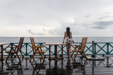 A young girl in a dress is standing in a sea restaurant. The island has rainy weather