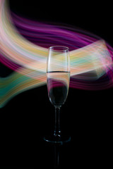 A single wine glass isolated on a black background with red white pink and orange neon light painting streaks of light behind them. Light wave, game of colors, drawing light.