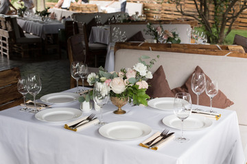 Wedding table setting decorated with fresh flowers in a brass vase. Wedding floristry. Banquet table for guests outdoors with a view of green nature. Bouquet with roses, eustoma and eucalyptus leaves