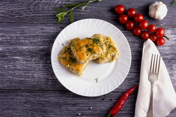 Delicious homemade casserole of zucchini, rice and cheese on a white plate on a wooden background.