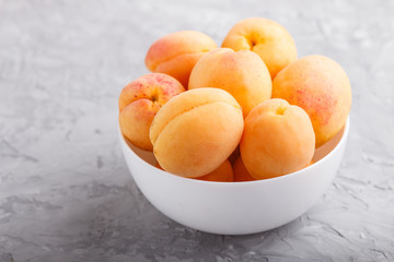 Fresh orange apricots in white bowl on gray concrete background. side view.