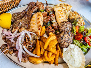 tasty dish with greek tzatziki sauce, a mixture of various types of grilled meat, chips and salad with onion and lemon for a meal - Powered by Adobe