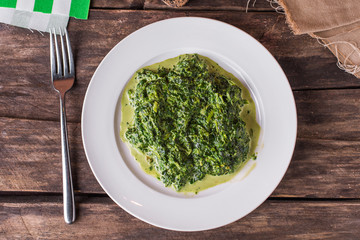 Cooked green spinach on a white plate on wooden table
