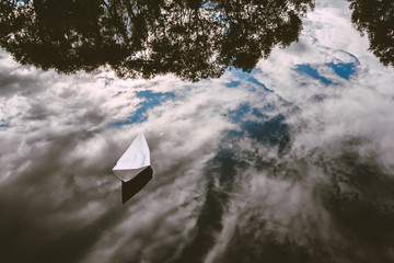 white paper boat on a pond. Ship is floating in the water with reflected sky