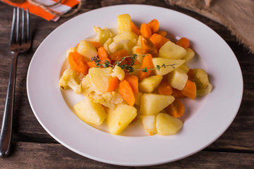 Boiled potatoes with vegetables and carrots on white plate on rustic wood table