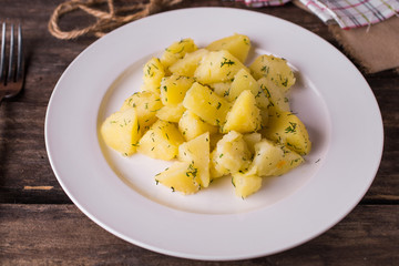Boiled potatoes with dill on white plate on rustic wood table