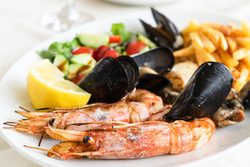 Seafood meal on the white dish plate cooked mussels shrimp or prawns with lemon and vegetables Mediterranean food