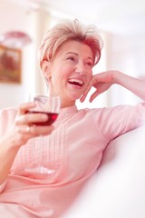 Obraz na płótnie Canvas Cheerful mature woman holding wineglass while looking away at home
