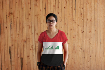 Woman wearing Iraq flag color shirt and standing with two hands in pant pockets on the wooden wall background.