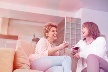 Cheerful mature friends with wineglasses sitting on sofa at home