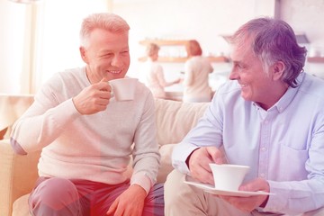 Smiling mature men holding coffee while sitting on sofa at home